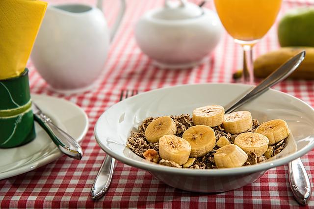 Bowl of granola with sliced bananas and glass of orange juice on table
