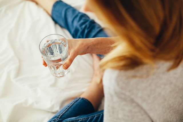 Woman sitting on bed drinking a glass of water