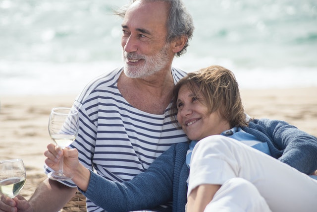 Older couple sitting on beach with wine glasses