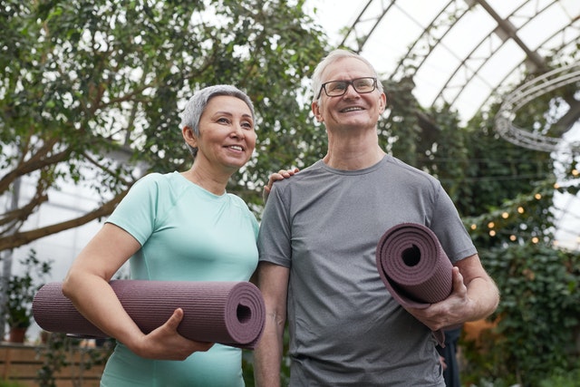 Older couple holding yoga mats standing in greenhouse