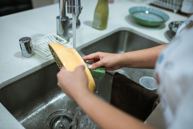 Closeup photo of someone washing a yellow bowl at a kitchen sink