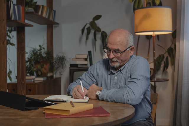 Older man sitting at table writing in a notebook