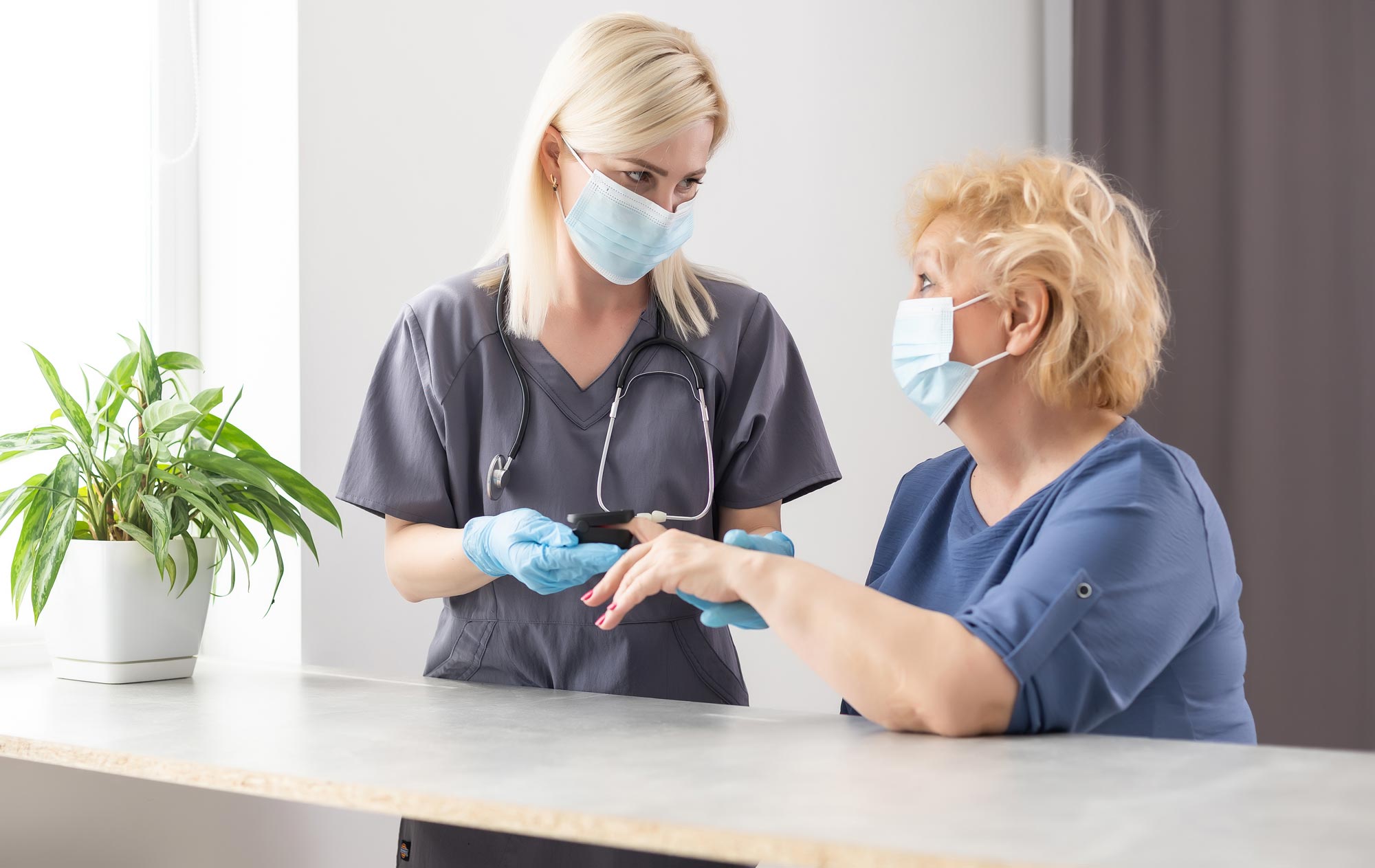  Woman doctor in a medical mask measures the patient's pulse and oxygen saturation to middle aged woman using a pulse oximeter