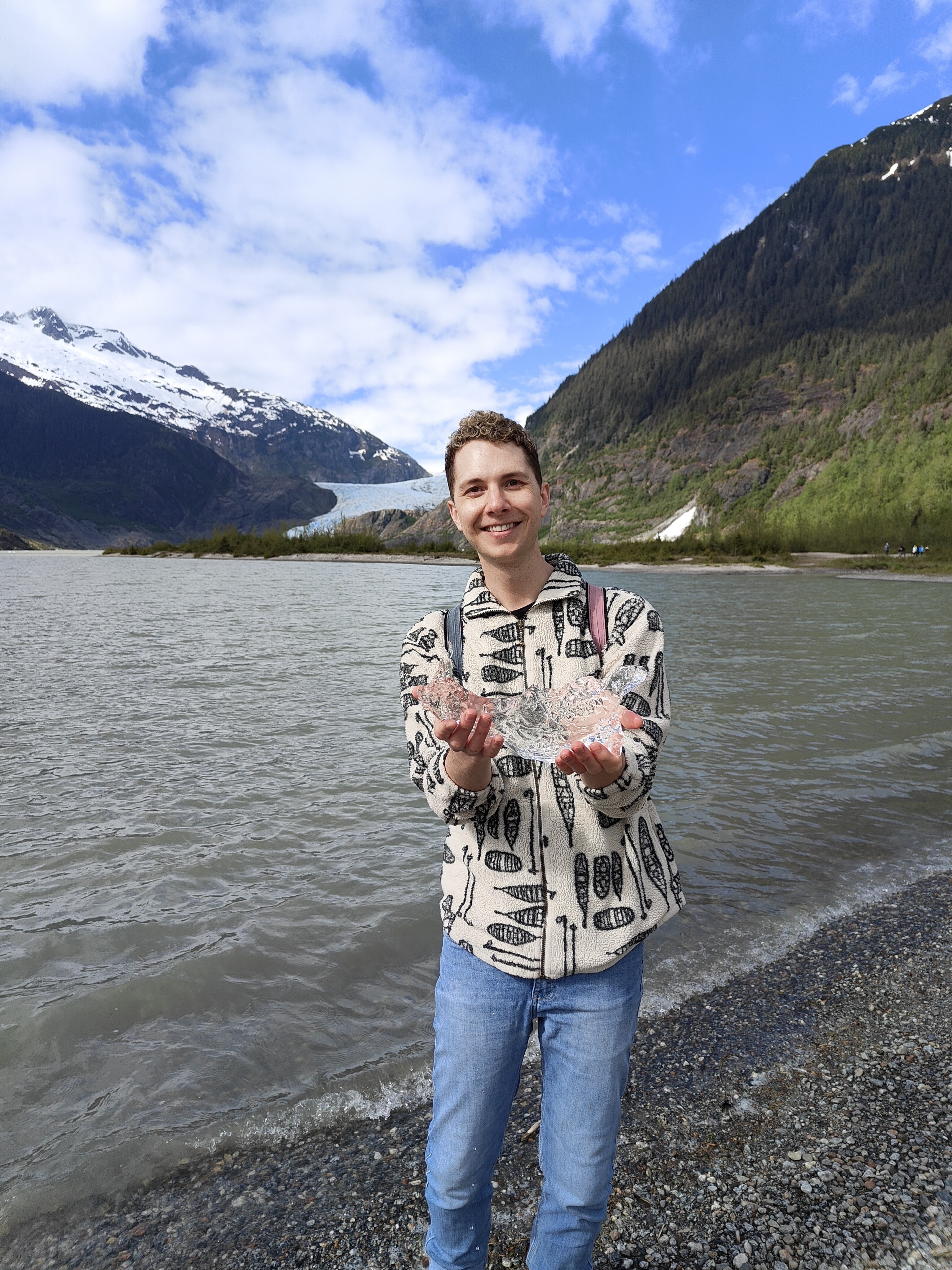 PhD student Justin Turner standing on the shore of a mountain lake