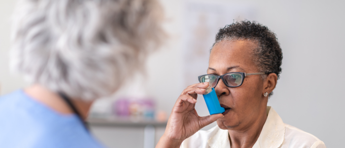 Older woman being supervised by nurse while using inhaler