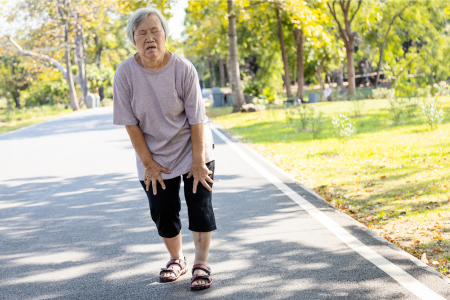 Older woman walking in park looking uncomfortable stops to catch her breath
