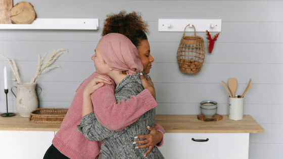 Woman hugging a second woman who is wearing a scarf over her head.